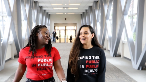 Two people walking in a hallway speaking to each other and smiling.