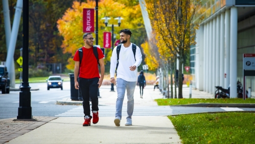 Two students walking in front of fall foliage