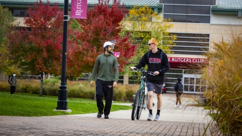 Two students walking and talking outside, with one rolling a bicycle 