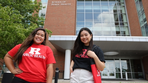Two students smiling in front of the Rutgers School of Public Health.
