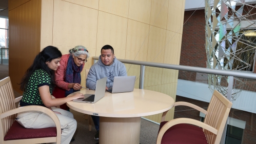 Professor helping two students working on laptops.