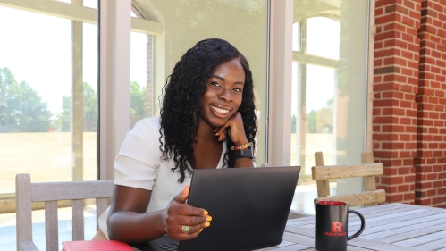 A student working on a laptop and smiling for the camera.