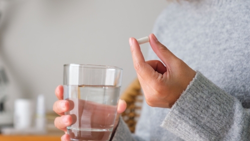 person holding pill and glass of water