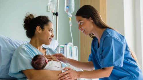 woman holding newborn baby in hospital with a nurse helping soothe the newborn