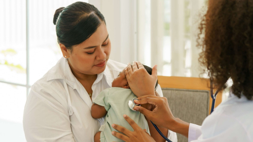 female nurse holding baby while female doctor performs infant examination
