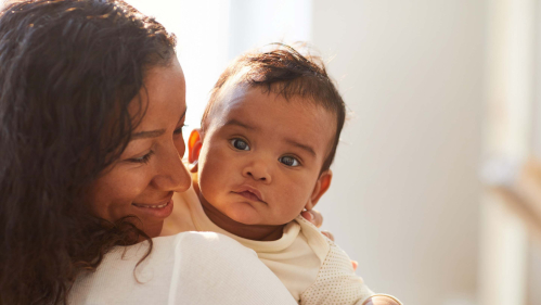 mother holding baby with the baby looking over the mother's shoulder