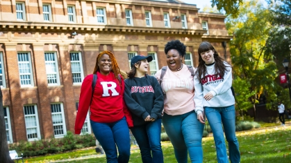Four students walk and laugh in front of Rutgers building.