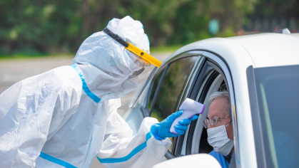 Person in car wearing mask and getting temperature checked. 