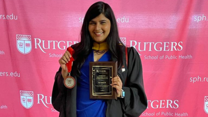 Graduate holding a medal and an award in front of a banner.