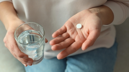 Hand holding pill and glass of water