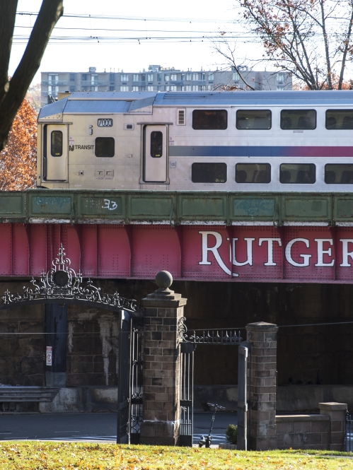 Train passing over red Rutgers bridge.