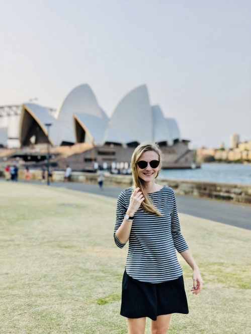 Person in sunglasses in front of Sydney Opera House looking at camera.