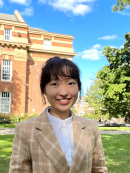 Headshot of person with bangs in front of building.