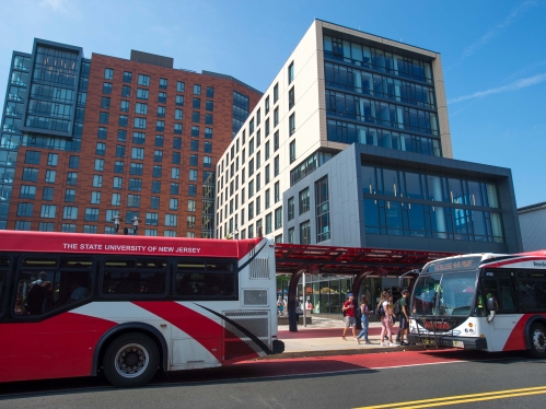 Red bus driving by tall buildings.