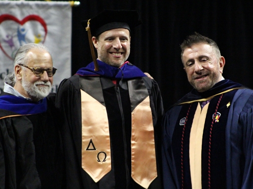 Three people on stage looking at the camera in graduation regalia.