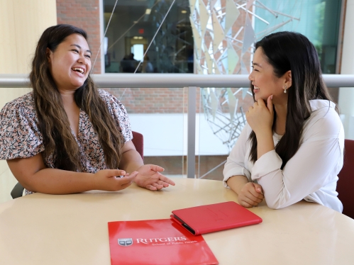 Two students talking while seated at a table.