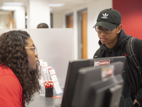 Two people talking, person on left in red shirt and person on right in black hoodie and hat