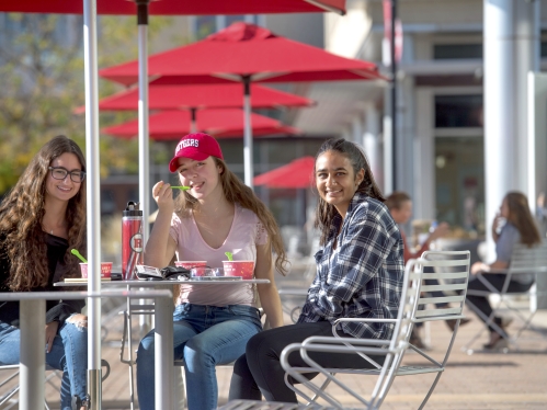 Three students dining on campus and smiling at camera.