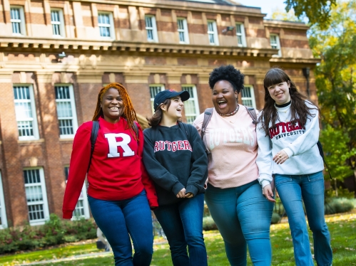 Four students walk and laugh in front of Rutgers building.