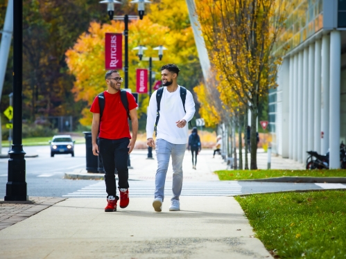 Two students walking in front of fall foliage 