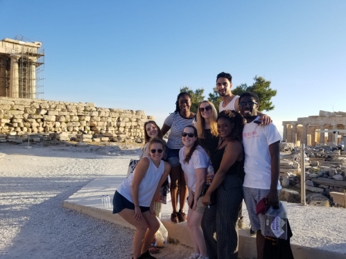 Seven people in front of Acropolis looking at camera.