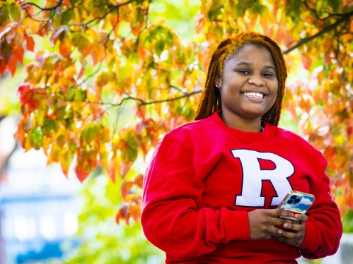Student with phone in hand smiling for camera.