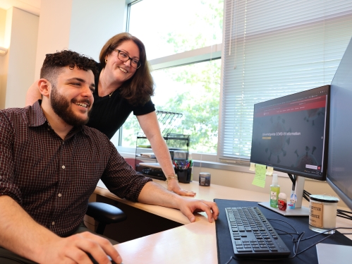 Two people smiling and working on a computer.