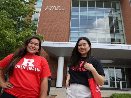 Two students smiling in front of the Rutgers School of Public Health.