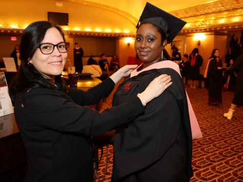 staff member helping graduate put on regalia