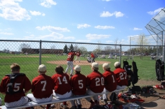 Baseball players sitting on bench watching teammate at bat.