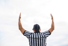 Referee holding up both arms with back to the camera.